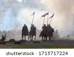Small photo of Reenactors riders on horses with spears and flags in the smoke of military operations.