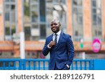 Small photo of Creative emotional Portraits of young mid-adult Kenyan black Male Man in suit white shirt stripped tie holding it smiling mildly in the streets of Nairobi City County Kenya East Africa Streets Style F