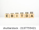 Small photo of EBITDA text written on wooden block with stacked coins on white background, growing trend, business concept. ebitda - short for earning before interest taxes depreciation and amortization