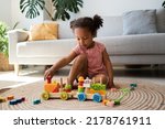 Small photo of Little black girl engaged in game, playing with wooden building railway station, resting on heating floor at home, enjoying comfort, leisure. African american child playtime and activity concept