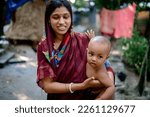 South asian young mother holding her baby son in a village environment, straw hatch in background, woman wearing shari 