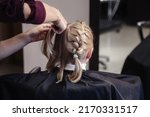 Small photo of Barber woman braids pigtails, makes fashionable pretty hairstyle for cute little blond girl child in barbershop. Hairdresser makes hairdo for young baby in barber shop. Concept hairstyle and beauty