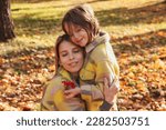 Mom and daughter in yellow coats spend time together in fall park outdoors, happy hugging. Adorable kid with rowan berries with mommy posing in autumn nature. Concept of mother day. Copy ad text space