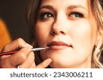 Small photo of Visagiste make makeup for lovely lady bride at wedding day in hotel room. Close-up of make-up artist with lips brush doing wedding makeup for woman. Concept of luxury wed service. Copy ad text space