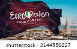 Small photo of Turin, Italy, January 2022: The flag of the Eurovision Song Contest 2022 logo waving in the wind with blurred landscape of Turin city. The 2022 edition will take place in Italy from 10 to 14 May