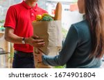 Small photo of smart food delivery service man in red uniform handing fresh food to recipient and young woman customer receiving order from courier at home, express delivery, food delivery, online shopping concept