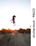 Small photo of freestyle BMX rider does dirt jump with sunset as background, turndown