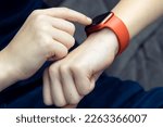Small photo of Unrecognizable teenager male hand typing on red smart watch on on wrist, time technology. Pulse heart checking, fitness tracker and cardiogram health application. Clock and Bluetooth technology