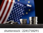 Small photo of Money of the United States and Europe and two Flags on a dark background. It is a symbol of the United States of America increasing tariff tax barriers for import products from EU countries.
