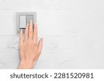 a woman's hand turns on or off the light with a light switch on a gray wall with copy space