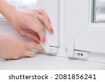 Small photo of Woman locks a child safety lock on a window frame an apartment on a high floor. Security lock for windows ensures the safety of your children and prevents accidents.