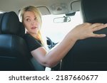 Small photo of Attractive blonde woman driving a car turned around to look out the rear window. The woman behind the wheel backs up. Driving, parking.