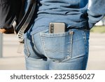 Small photo of Smartphone sticks out of the back pocket of jeans. The woman put her cell phone in the back pocket of her jeans. The concept of pickpocketing, indiscretion, frivolity.
