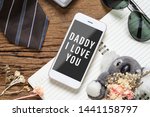 Father's day background concept. Mock up mobile phone for your artwork with Father's accessories items and daughter's toy on wood with Dady I love you messages on smartphone.