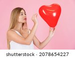 Small photo of Young latina woman playing with a heart-shaped balloon. With a needle about to break the heart, valentine concept. Woman angry with love. Concept of revenge in love.