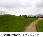 On the left is a green grassy hill and near it a dirt path against a gray sky with clouds