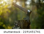 Small photo of An axe with a wooden handle is stuck into a wooden stump. Axes in the rays of the setting sun in the forest.