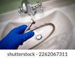 The master's gloved hand holds a chrome bathroom hose.Call the master plumber.