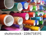 Small photo of Rolls of multicolored vinyl film on the shelves. Self-adhesive film for pasting shop windows and vehicles.External tuning of the car. Workshop for the production of outdoor advertising.