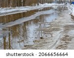 Small photo of A road with melting snow, puddles and ice on a cloudy spring day. Reflections in cold water. Snow and mud. Thawed patches. Spring has come, the month of March.