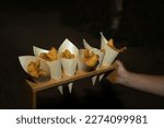 Small photo of Presentation of small paper cones filled with dogfish in marinade during a catering. Food concept, menu, catering.