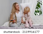 Small photo of Mom brushing her daughter's hair. A funny little girl is cranky next to her parent. Mom can't brush her blond daughter's hair