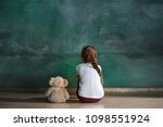 Little autistic girl with teddy bear sitting on floor at empty room. Autism concept. Conceptual image with little caucasian model at studio. Back view