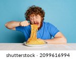 Small photo of Crazy dish. Emotional young hairy red-bearded man tasting large portion of noodles, pasta isolated on blue studio background. Food, festival, ad, popularity, taste and dieting. Healthy carbohydrates.