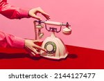 White telephone, Pop art photography. Retro objects, gadgets. Female hand holding handset of vintage phone isolated on pink and red background. Vintage, retro 80s, 70s style. Complementary colors.
