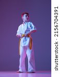Small photo of Champion. Serious kid, little boy, taekwondo or karate athletes in doboks posing isolated on very peri color background in neon. Concept of sport, education, skills, martial arts, healthy lifestyle