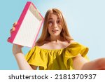 Wow, surprised emotions. Wide angle bottom view of young beautiful astonished girl holding gift box isolated on blue background. Concept of joy, holidays, inspiration, sales, ad. Happiness.