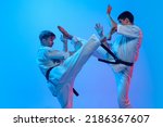 Karate fight. Studio shot of sports training of two karatedo fighters in doboks isolated on blue background in neon. Concept of combat sport, challenges, skills. Sportsmen practicing base technique