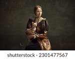 Small photo of Portrait of pretty young girl in elegant retro clothing over dark vintage background posing with sphynx cat. Lady with ermine remake. Concept of history, renaissance art remake, comparison of eras
