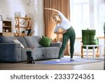 Senior beautiful woman in comfortable sportswear training at home, doing warming-up and stretching exercises. Concept of sportive and healthy lifestyle, age, body care, fitness, wellness.