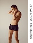 Small photo of Handsome, shirtless, muscular young man fit fit body standing in underwear, holding hand on neck against grey studio background. Concept of men's beauty, health, body care, sportive lifestyle