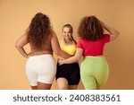 Small photo of Three smiling young omen, plus size models in comfortable sportswear over beige studio background. Concept of sport, body-positivity, weight loss, body and health care