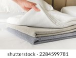 Small photo of woman puts fresh clean towels on the bed in a hotel guest room, close-up. Woman's hand touches soft terry towels after cleaning the room