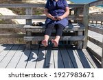 Senior woman is holding her wet feet up in the sun to dry off, causing a shadow on the deck below. Waiting for the water to evaporate.