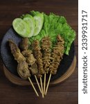 Small photo of indonesian traditional satay named sate jeroan consist of chicken offal, chicken skin, chicken intestine, chicken liver gizzard, kikil or cow hide on a black plate on the wooden table.