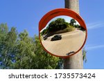 Small photo of Road round mirror. Mirror to help transport. Help cornering. Red round mirror on a post. Road mirror on a background of blue sky. Give Way.