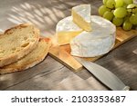 French camembert of Normandy served on wooden cutting board with grapes and slices of bread.