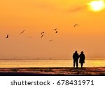 Old couple walking near the sea at sunset. The Sun between clouds and seagulls flying on the sea, silhouette. 