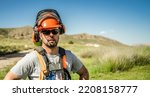 Small photo of Portrait of a workerman wearing helmet, ear muffs, harness and sunglasses, looking at the camera, during a sunny spring afternoon outdoors.