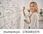Beautiful blonde lady looking at camera and smiling while standing in front of planner whiteboard at work