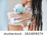 Close up of lady with foam on her skin using bath loofah while taking shower at home