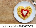 Heart shaped spaghetti with tomato sauce and parmesan cheeses on white plate with wooden background.Healthy vegeterian romantic art food idea for Valentine's dinner.Top view.Copy space

