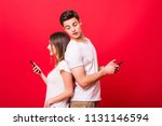 Small photo of Beautiful woman and handsome man with smart phones spu each other over red background