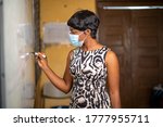 Small photo of image of class teacher writing on marker board-black lady tutor in face mask after lock down-beautiful African madam with short hair in lecture room