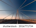 Linear perspective view of a white cable-stayed suspension bridge in the golden light of the rising sun shot from a ground level in horizontal (landscape) format