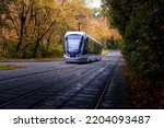 A modern-style tram goes out of a dense forest in autumn colours, Moscow, Russia